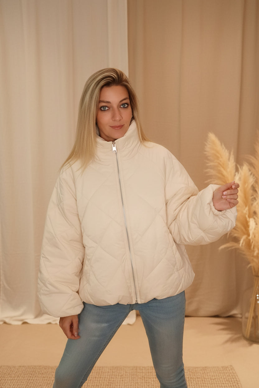 Frau in cremeweißer, gesteppter Boho-Luxe Jacke aus weichem Material und blauen Jeans