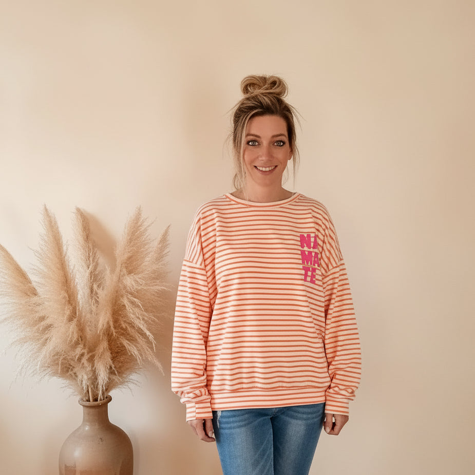 Frontansicht des peach-weiß gestreiften NAMASTE-Sweatshirts mit langen Ärmeln und pinkem Brustprint