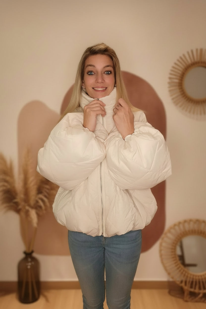 Frau in weißer, gesteppter Pufferjacke aus glänzendem Material und blauen Jeans im Boho-Luxe Stil.