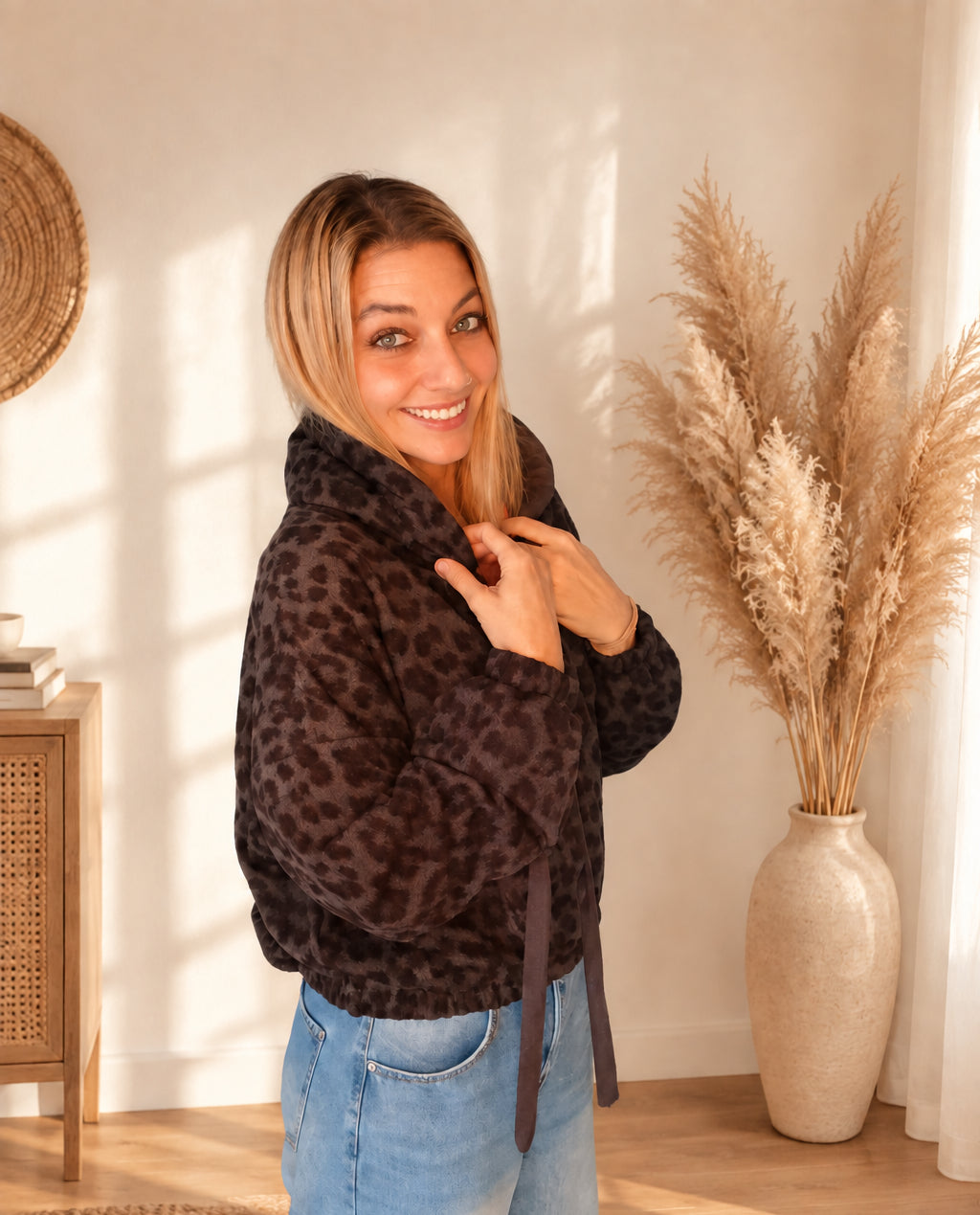 Damen-Hoodie mit dunklem Leomuster in seitlicher Ansicht, mit Händen an der Kapuze und sichtbaren breiten Bindebändern.