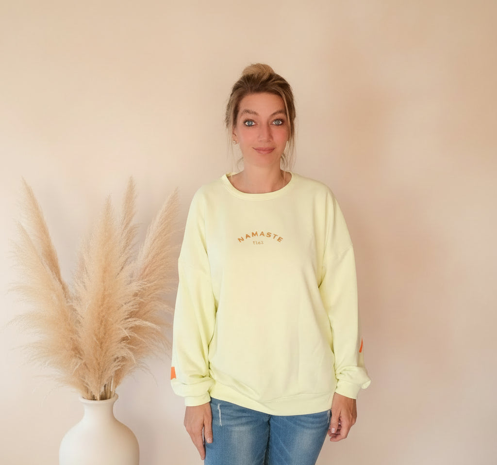 Namasté Oversize Sweatshirt Damen Pastellgelb – Frontansicht Ganzkörper lächelnd Namasté 24/7 Frontprint Neonorange Ärmelprint Pampagras