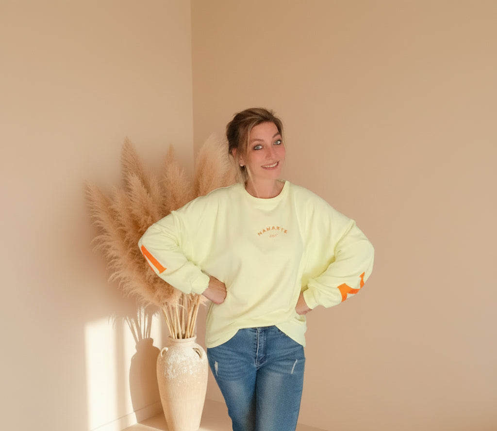 Namasté Oversize Sweatshirt Damen Pastellgelb – Frontansicht Hände in Hüften lächelnd Neonorange Ärmelprint warmes Boho Setting