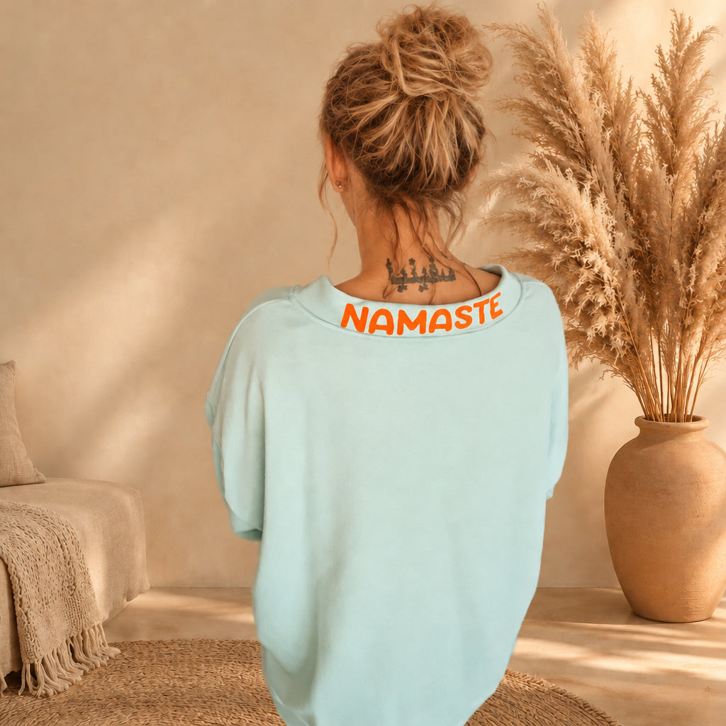 Nahaufnahme der Rückseite des mintfarbenen Pullovers mit orangefarbenem Namasté-Schriftzug am Ausschnitt