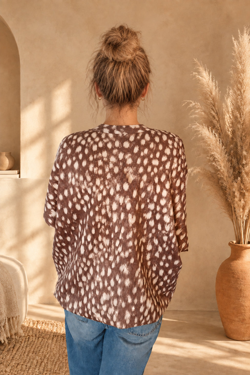 Rückansicht der Damenjacke mit Fleckenmuster in Braun-Creme, am Model mit Dutt und gesenkten Armen.