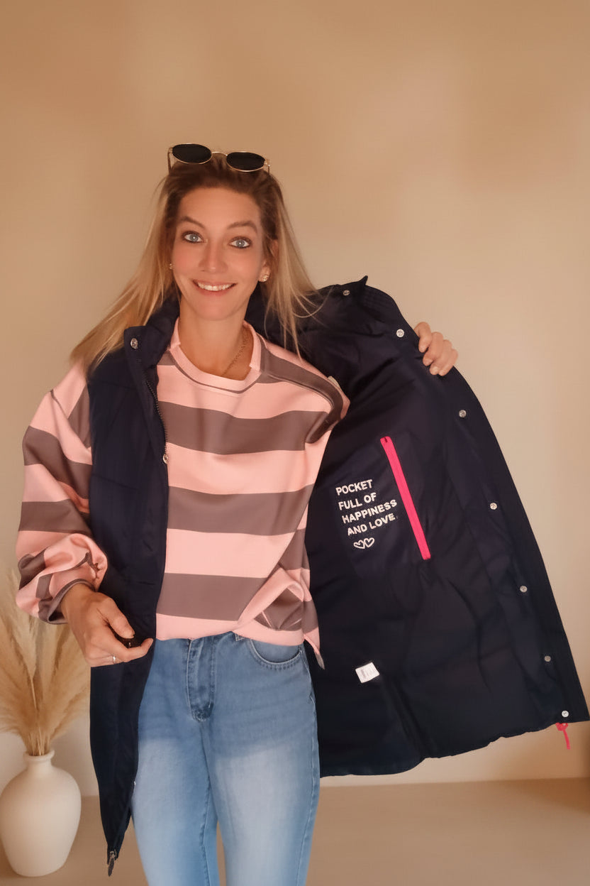 Frau in rosa-grau gestreiftem Oberteil und dunkelblauer Funktionsjacke mit Jeans.