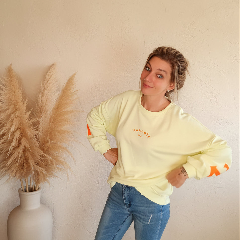Namasté Oversize Sweatshirt Damen Pastellgelb – lässige Pose Hände in Hüften lächelnd Neonorange Ärmel- und Frontprint Pampagras