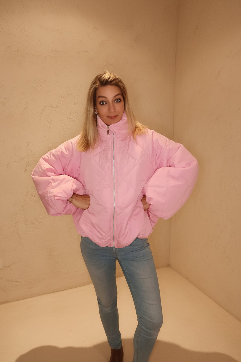 Frau in einer rosa Steppjacke aus glänzendem Material und blauen Jeans im Boho-Luxe Stil.