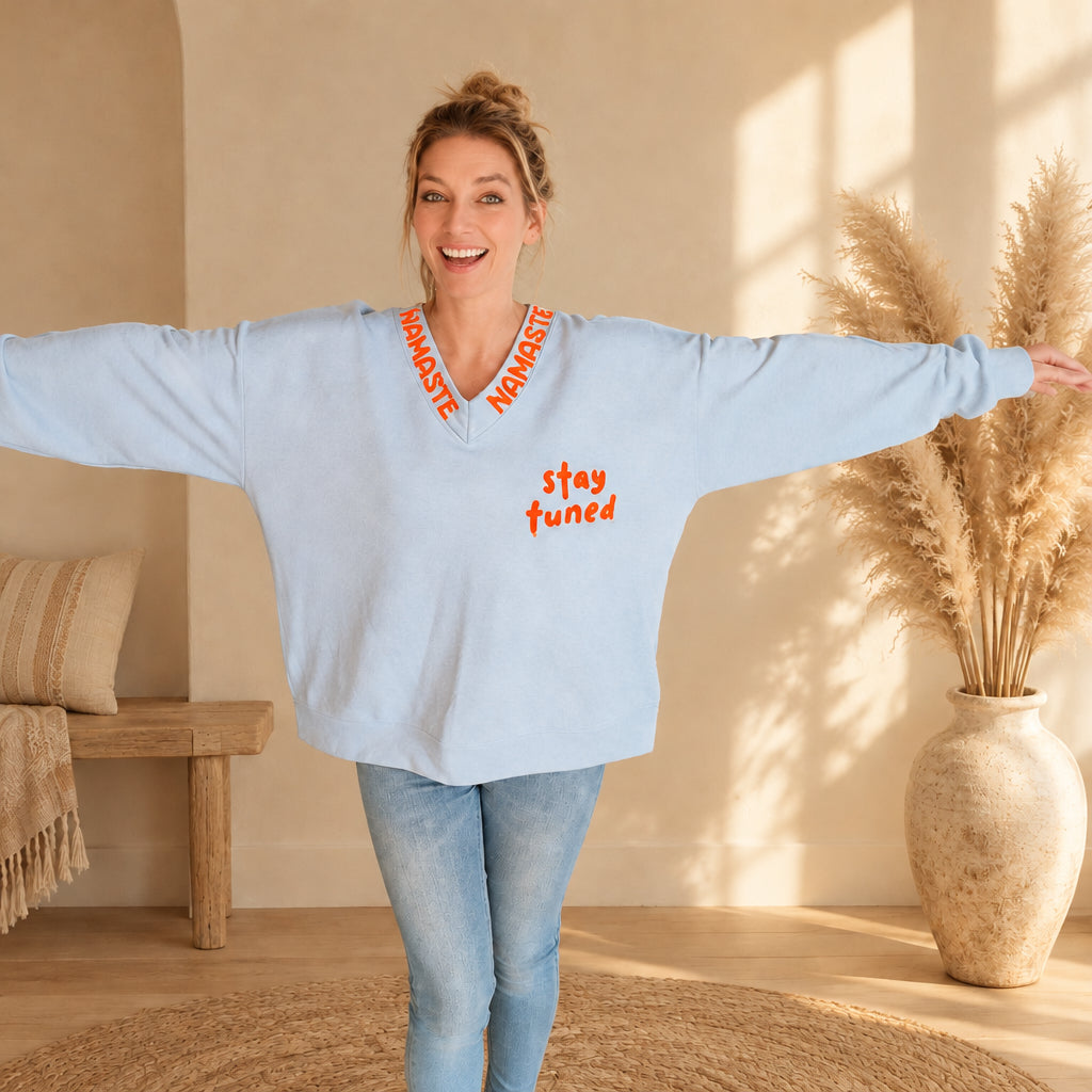 Weit geschnittener hellblauer Namaste-Pullover mit „stay tuned“-Print, Frontansicht mit ausgestreckten Armen