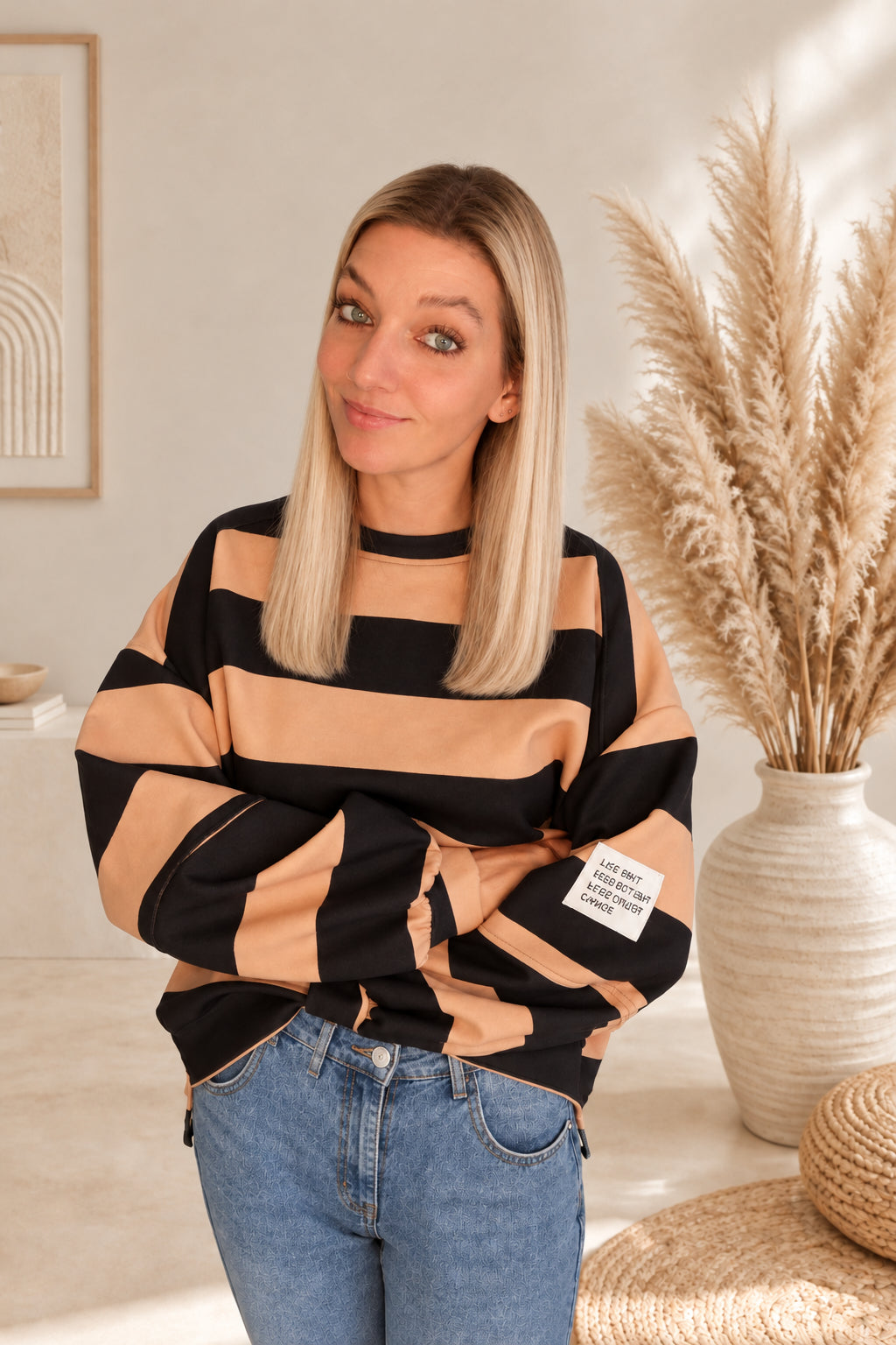 Damen-Sweatshirt mit Streifen in Camel und Schwarz, am Model mit verschränkten Armen und sichtbarem Ärmelpatch.