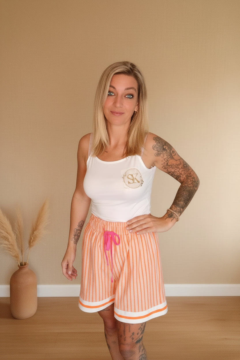 Damen Sommer-Shorts Orange Streifen – lächelnde Frontansicht, heller Hintergrund mit weißer Vase