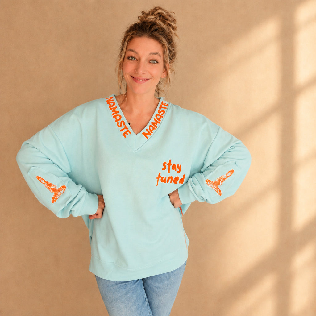 Damenpullover in Mint mit orangefarbenen Schriftzügen am V-Ausschnitt und lockerem Saum, Frontansicht