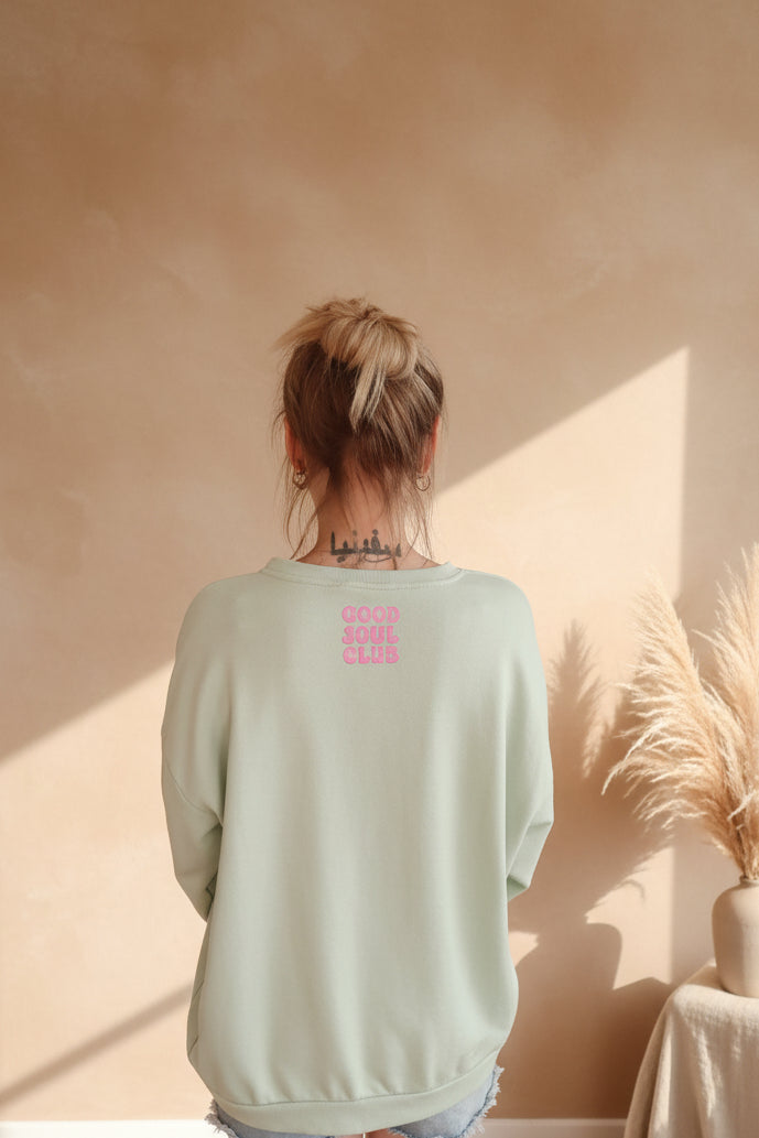 Hellgrüner Boho-Luxe Sweatshirt aus weichem Stoff mit rosa Aufdruck auf dem Rücken.