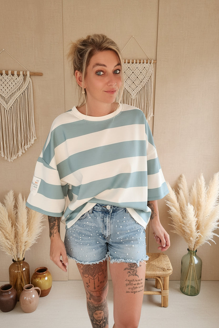 Boho-Luxe Look: Weiß-blau gestreiftes Oversize-Shirt aus Baumwolle und Denim-Shorts mit Perlen.