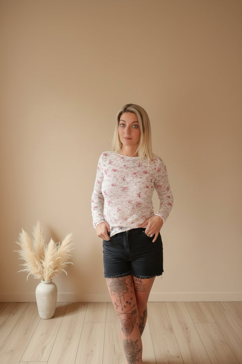 Boho-Luxe Damenmode: Weißes Langarmshirt mit floralem Muster und schwarzen Shorts.