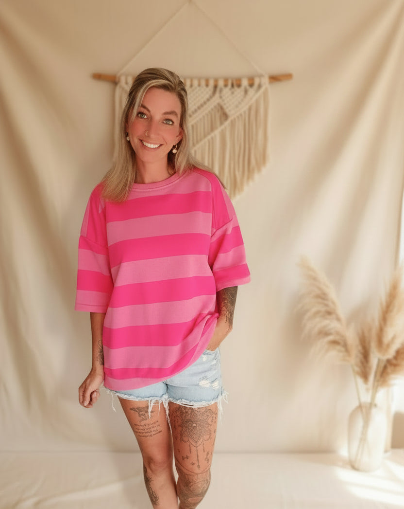 Oversize T-Shirt Pink Hellpink Gestreift – Frontansicht lächelnd, kombiniert mit Jeans-Shorts, Boho-Makramee-Hintergrund