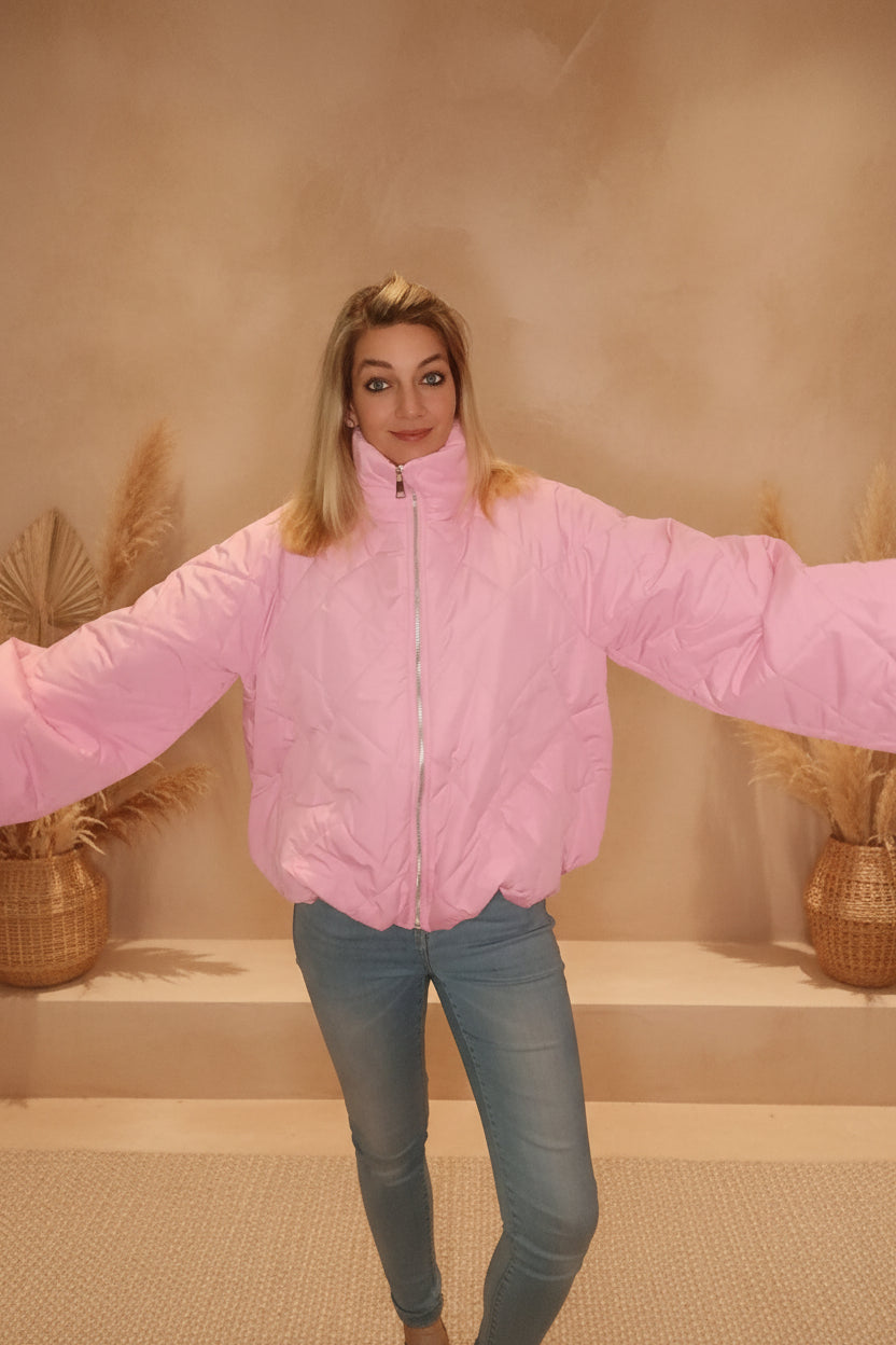 Frau in einer rosa gesteppten Pufferjacke aus synthetischem Material und hellblauer Jeans.