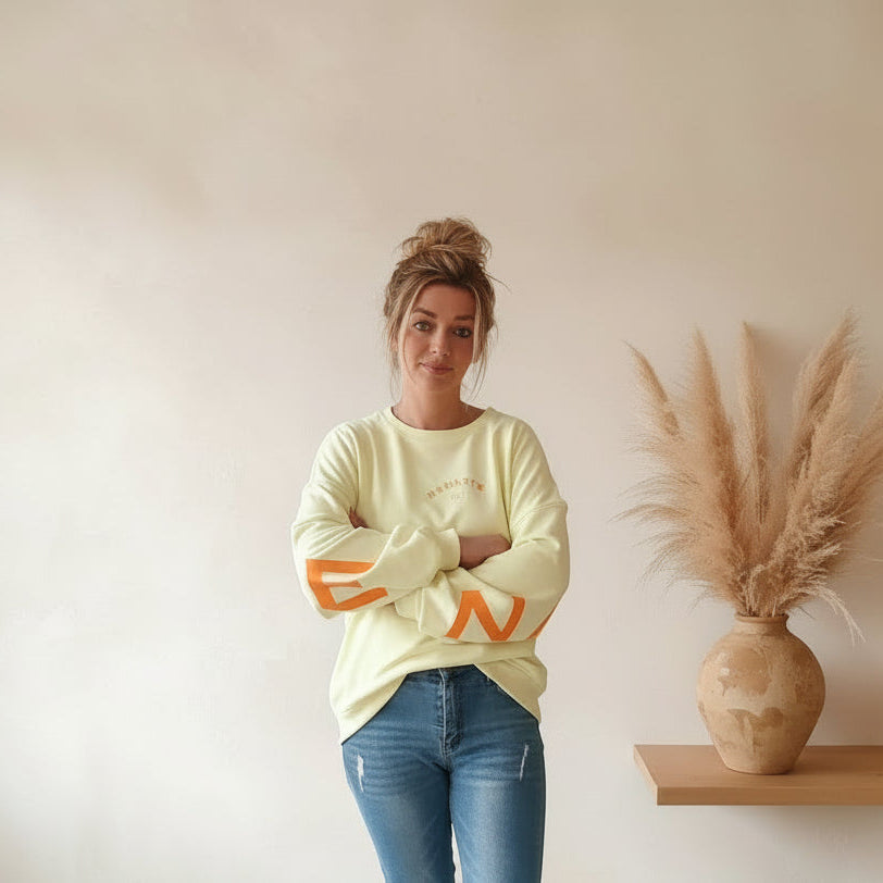 Namasté Oversize Sweatshirt Damen Pastellgelb – Frontansicht Arme verschränkt lächelnd Neonorange Ärmelprint Pampagras