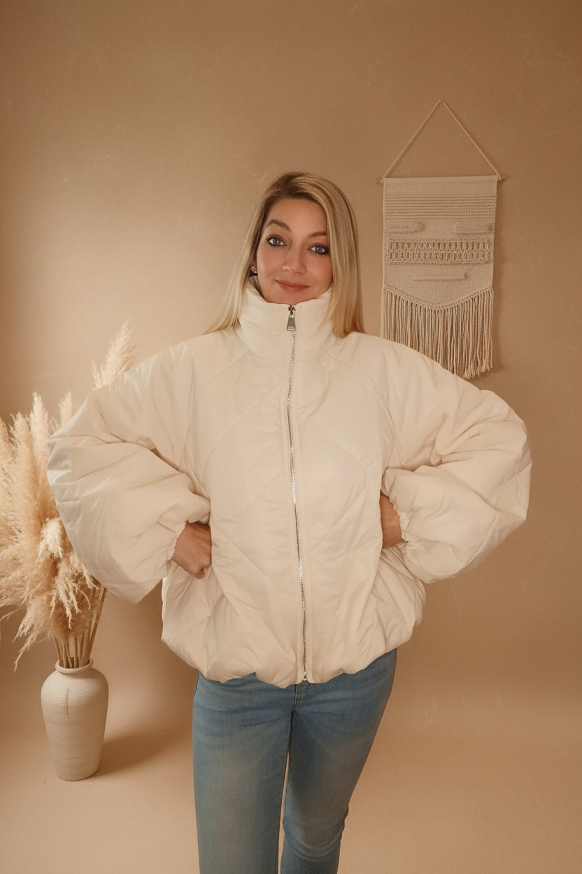Frau in cremeweißer, oversized Steppjacke aus glattem Material im Boho-Luxe Stil.