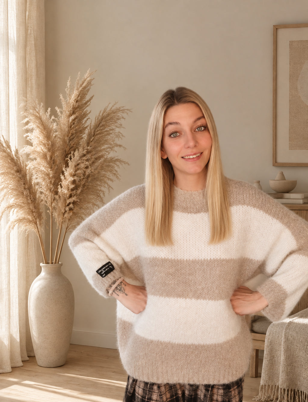 Frontansicht des beige-creme gestreiften Damen-Strickpullovers mit weiten Ärmeln, Hände an der Taille