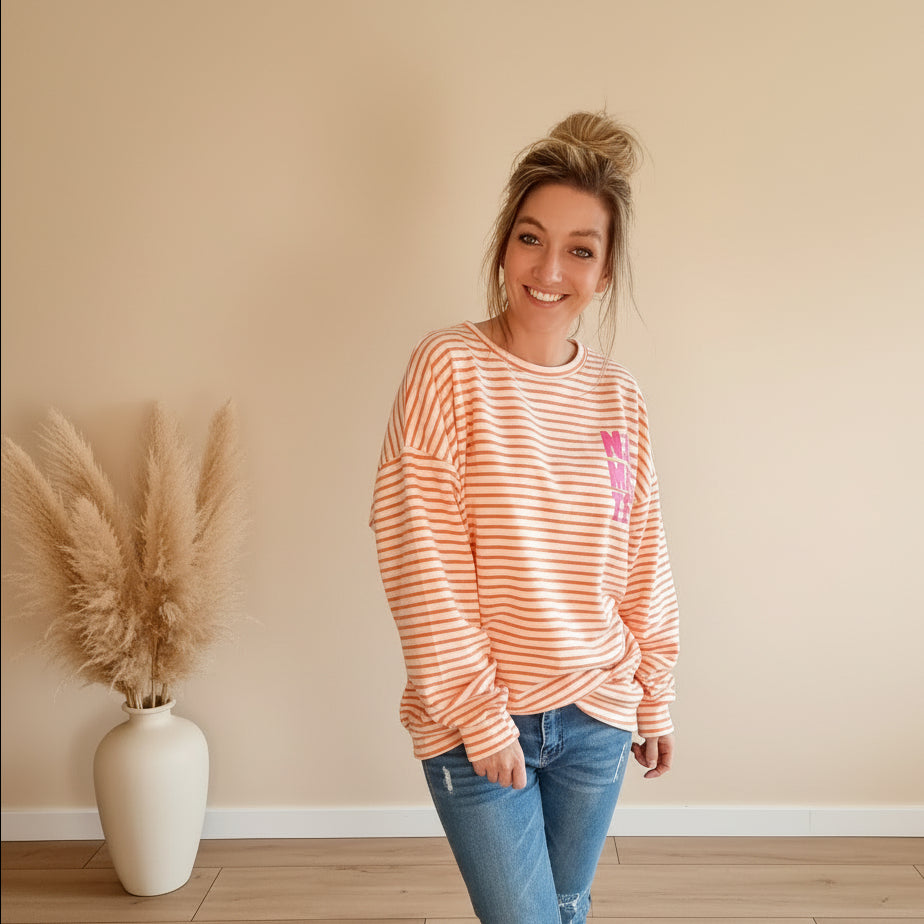 Damen trägt peach-weiß gestreiftes Oversize-Sweatshirt mit pinkem Print und Jeans
