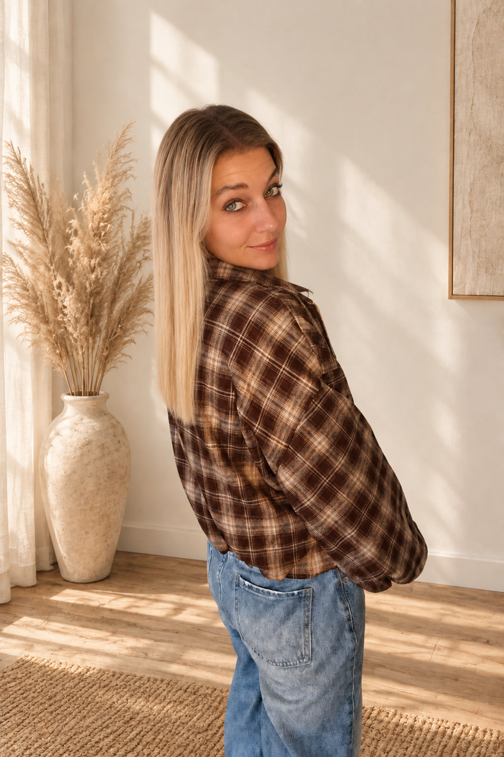 Schräge Rückansicht einer kurzen karierten Damenjacke in Dunkelbraun und Beige, getragen zu blauer Jeans.