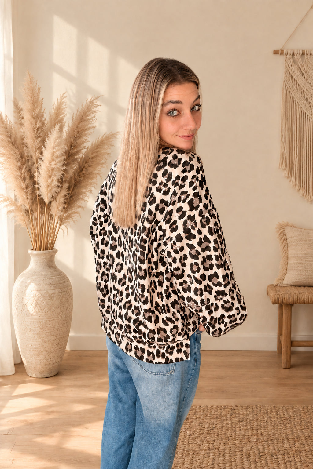 Seitliche Rückansicht des Damen-Oberteils mit Leoprint und weiten Ärmeln, am Model zur blauen Jeans mit Blick über die Schulter.