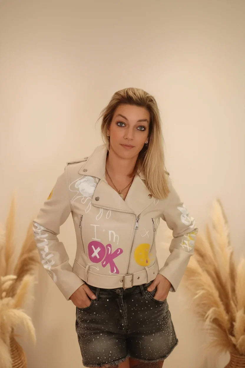 Frau in beiger Lederjacke mit bunten Graffiti-Prints und dunklen Denim-Shorts im Boho-Luxe Stil.