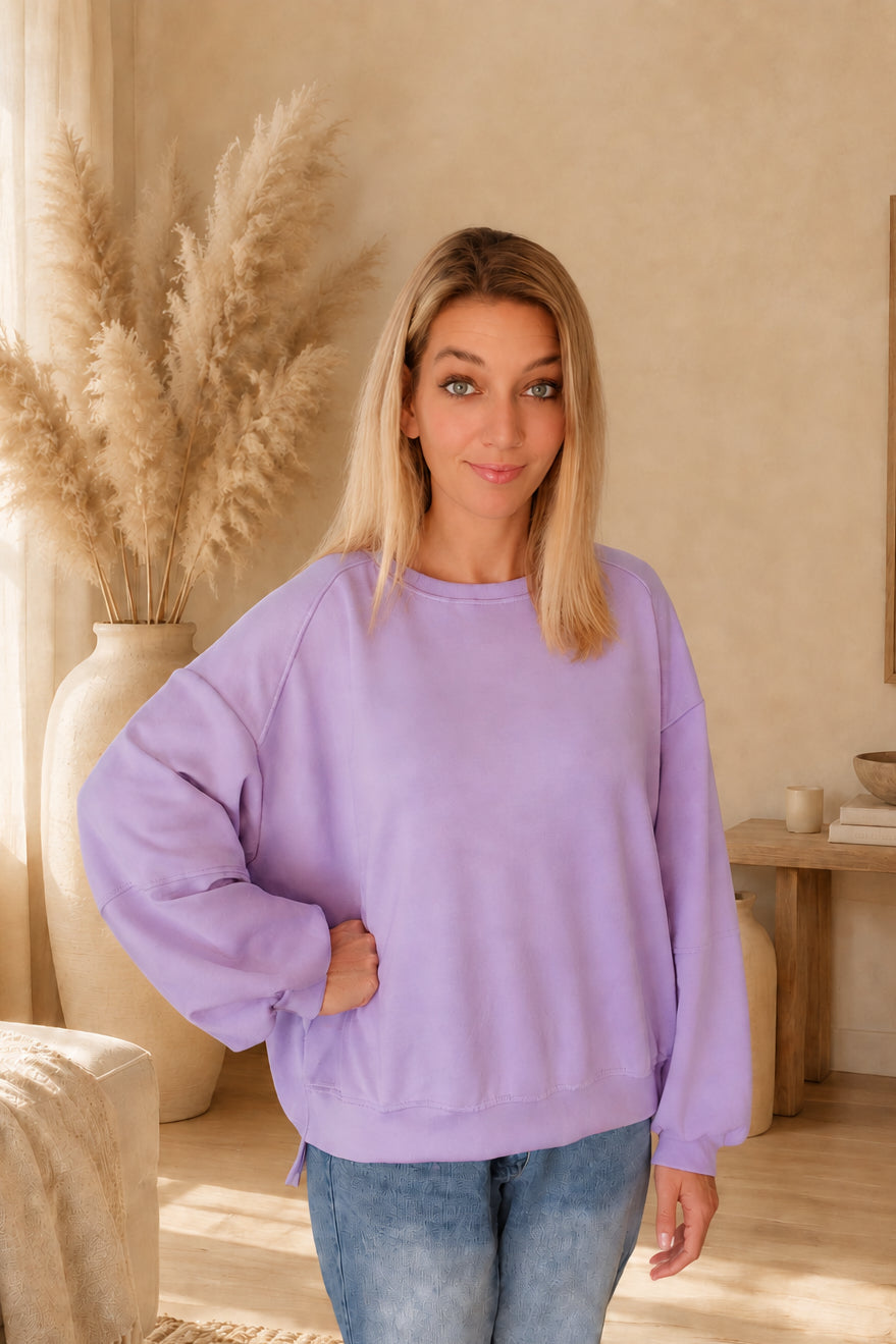 Fliederfarbenes Damen-Sweatshirt mit Rundhalsausschnitt und langen Ärmeln, am Model mit einer Hand an der Hüfte und vollständig sichtbarem Saum.