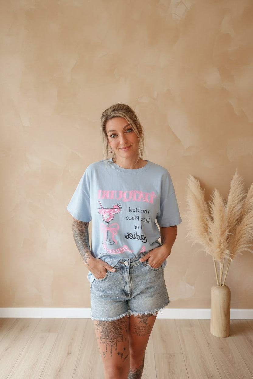 Boho-Luxe Look: Frau im hellblauen T-Shirt und Denim-Shorts vor beigem Hintergrund.