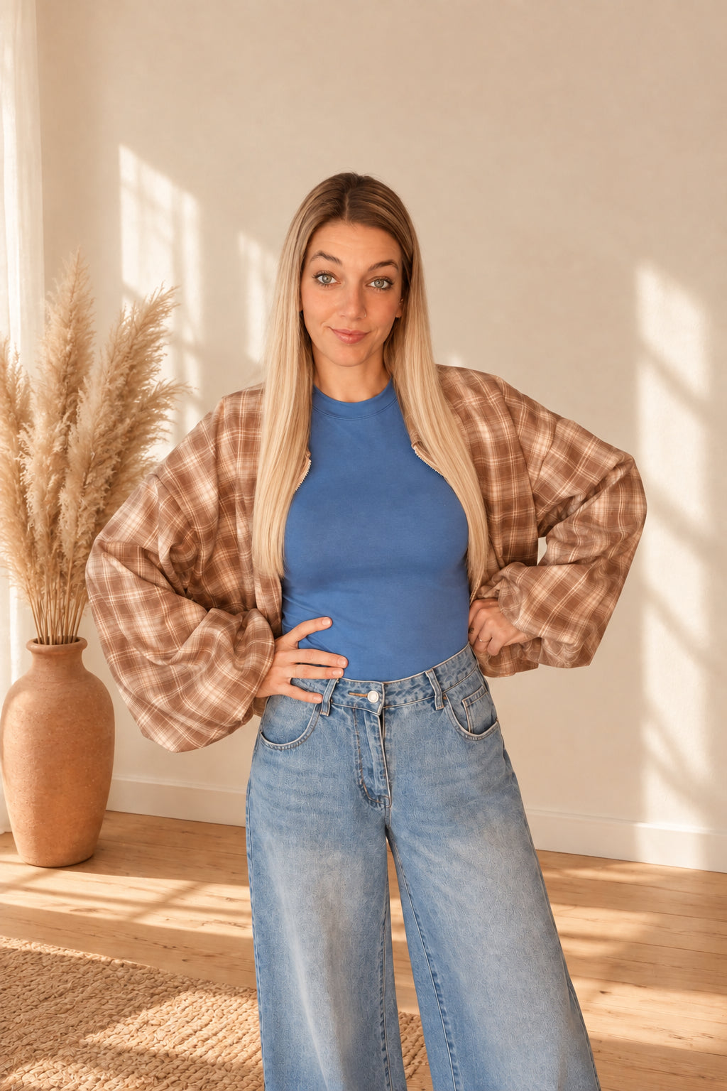 Karierte Damenjacke in Braun und Creme, offen über einem blauen Shirt getragen, mit Händen an der Hüfte.
