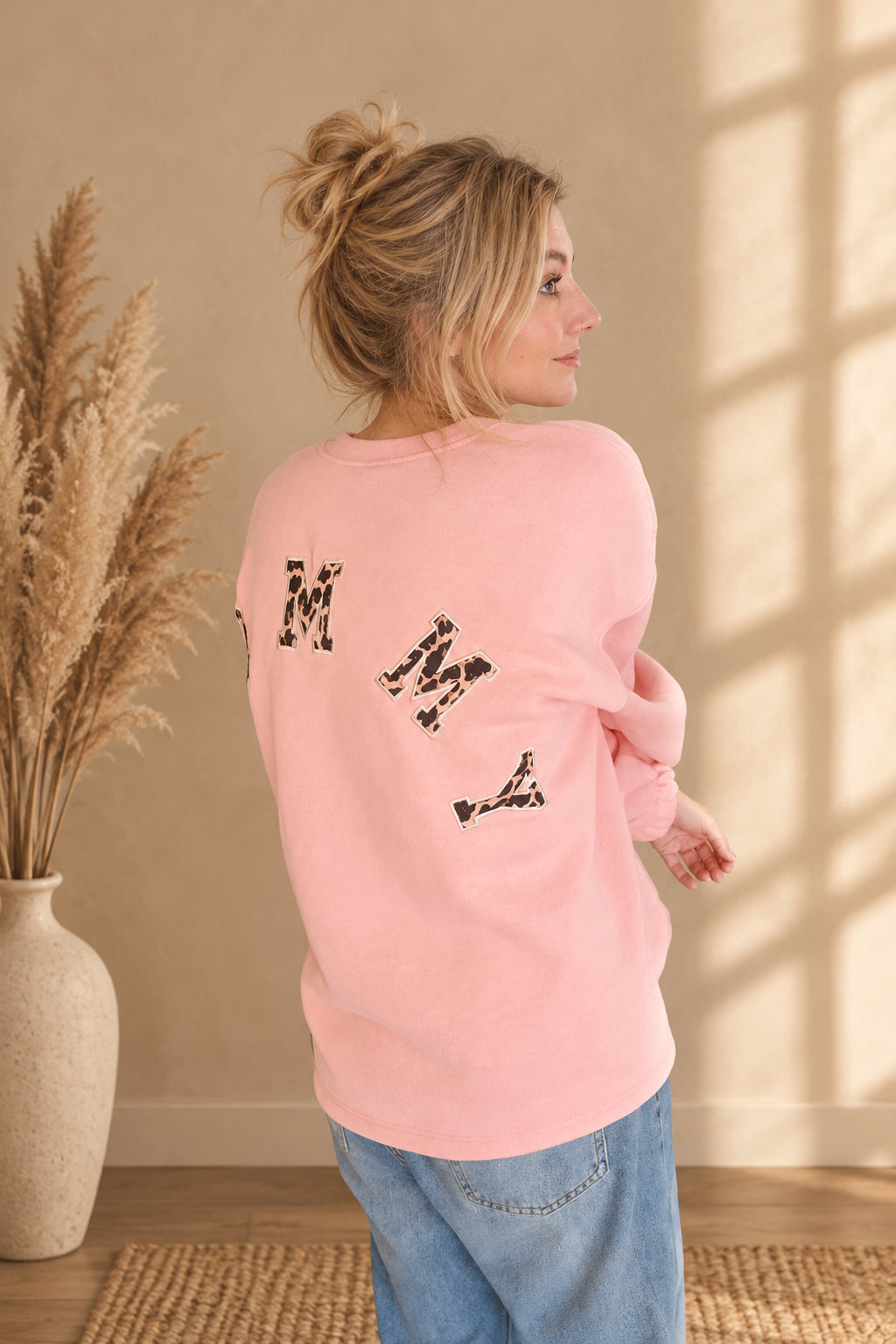 Rosa Damen-Sweatshirt mit Leomuster-Buchstaben auf dem Rücken, in seitlicher Rückansicht am Model.