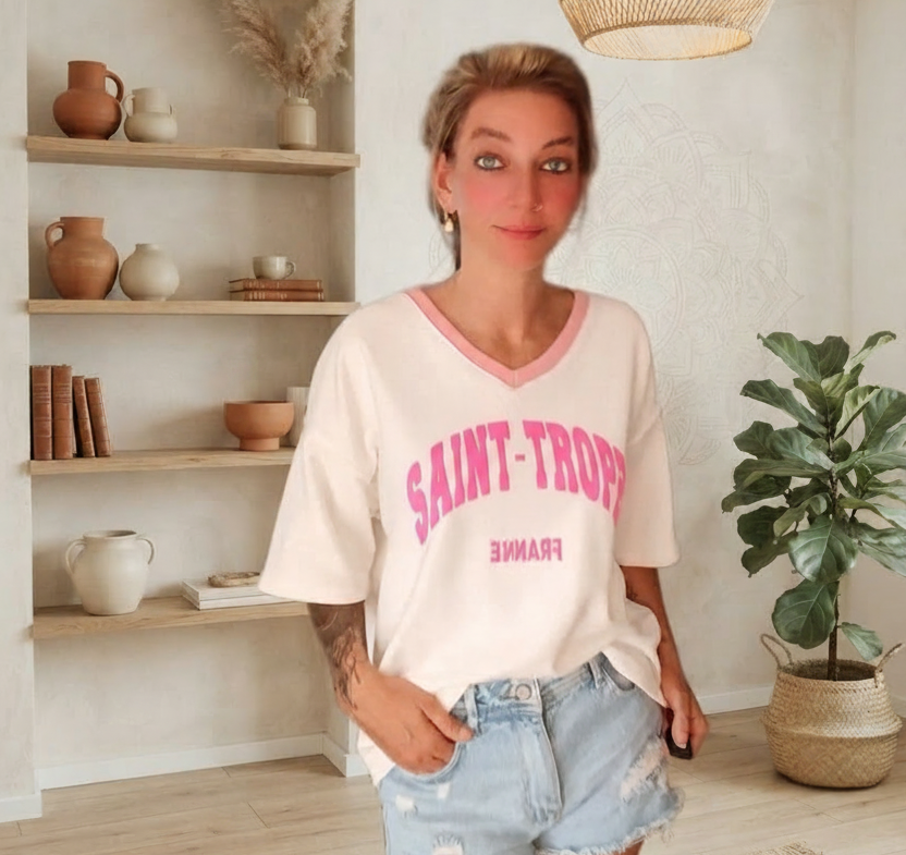 Frau in einem hellrosa V-Ausschnitt T-Shirt mit Saint-Tropez-Aufdruck und hellen Jeansshorts.