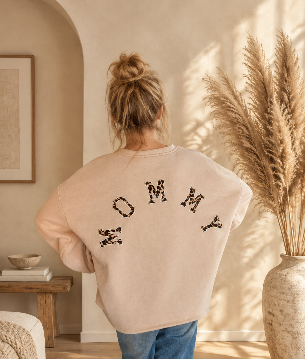 Damen-Sweatshirt in Creme mit großem MOMMY-Schriftzug im Leomuster auf dem Rücken, am Model mit Händen an der Hüfte.