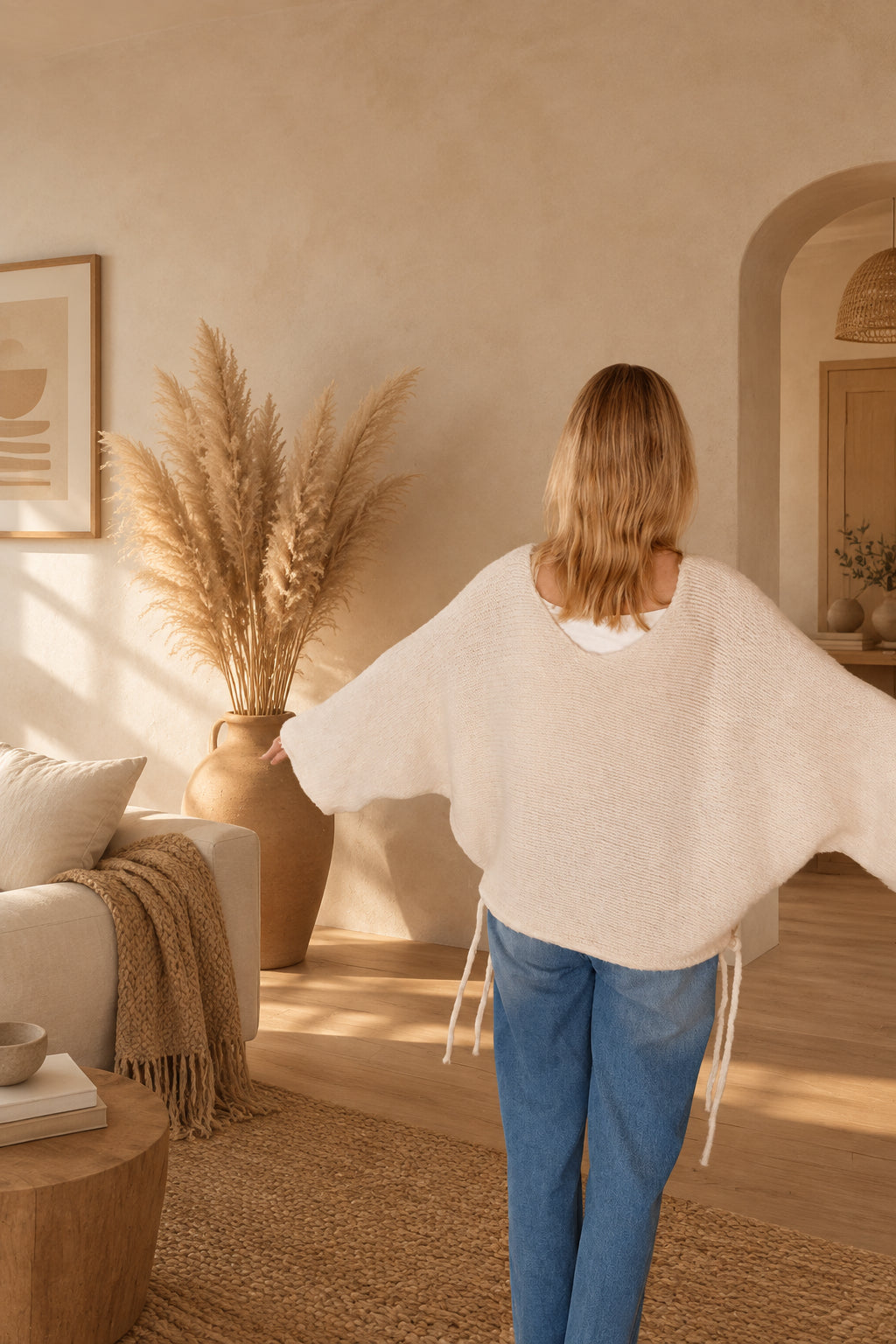 Rückansicht eines cremeweißen Oversized-Sweaters mit weiten Ärmeln und seitlich herabhängenden Bändern am Model.