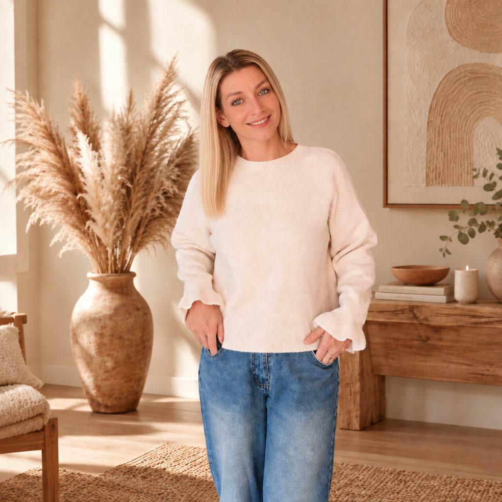 Model trägt einen hellen Damenpullover zu blauen Jeans, die Hände locker an den Hosentaschen.