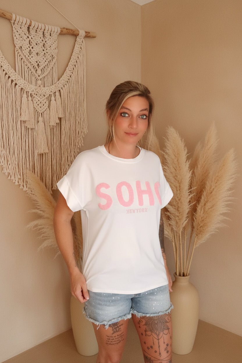 Boho-Luxe Style: Frau in weißem Baumwoll-T-Shirt mit SOHO-Print und hellblauen Jeans-Shorts.