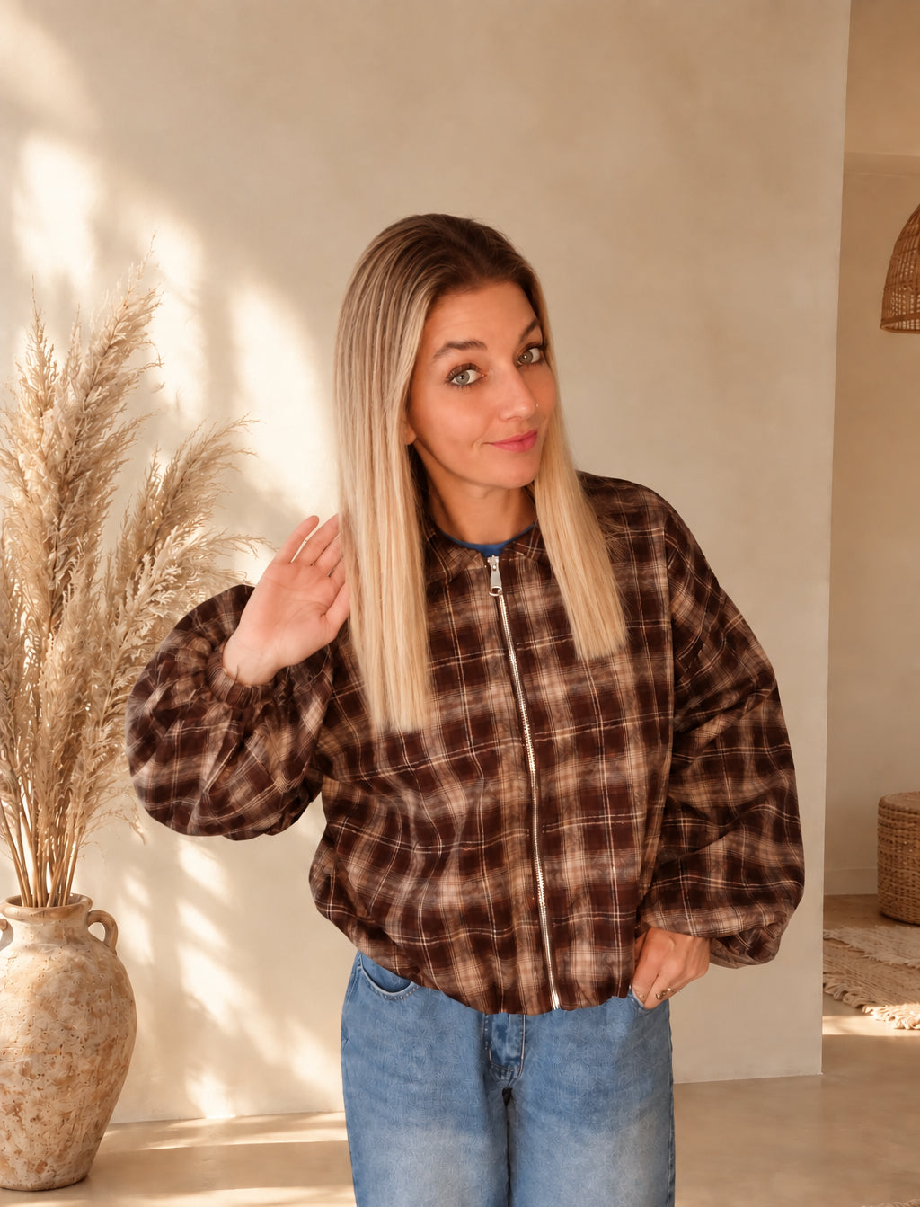 Geschlossene karierte Damenjacke in Dunkelbraun und Beige, Model mit einer erhobenen Hand und einer Hand an der Hüfte.