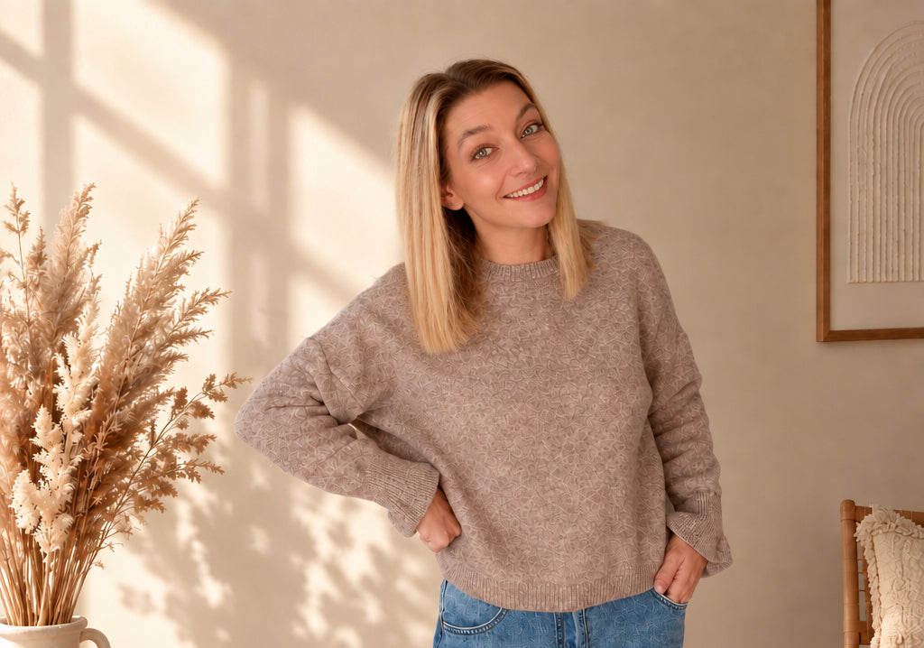 Model trägt einen taupefarbenen Damenpullover zu Jeans und steht mit einer Hand an der Hüfte.