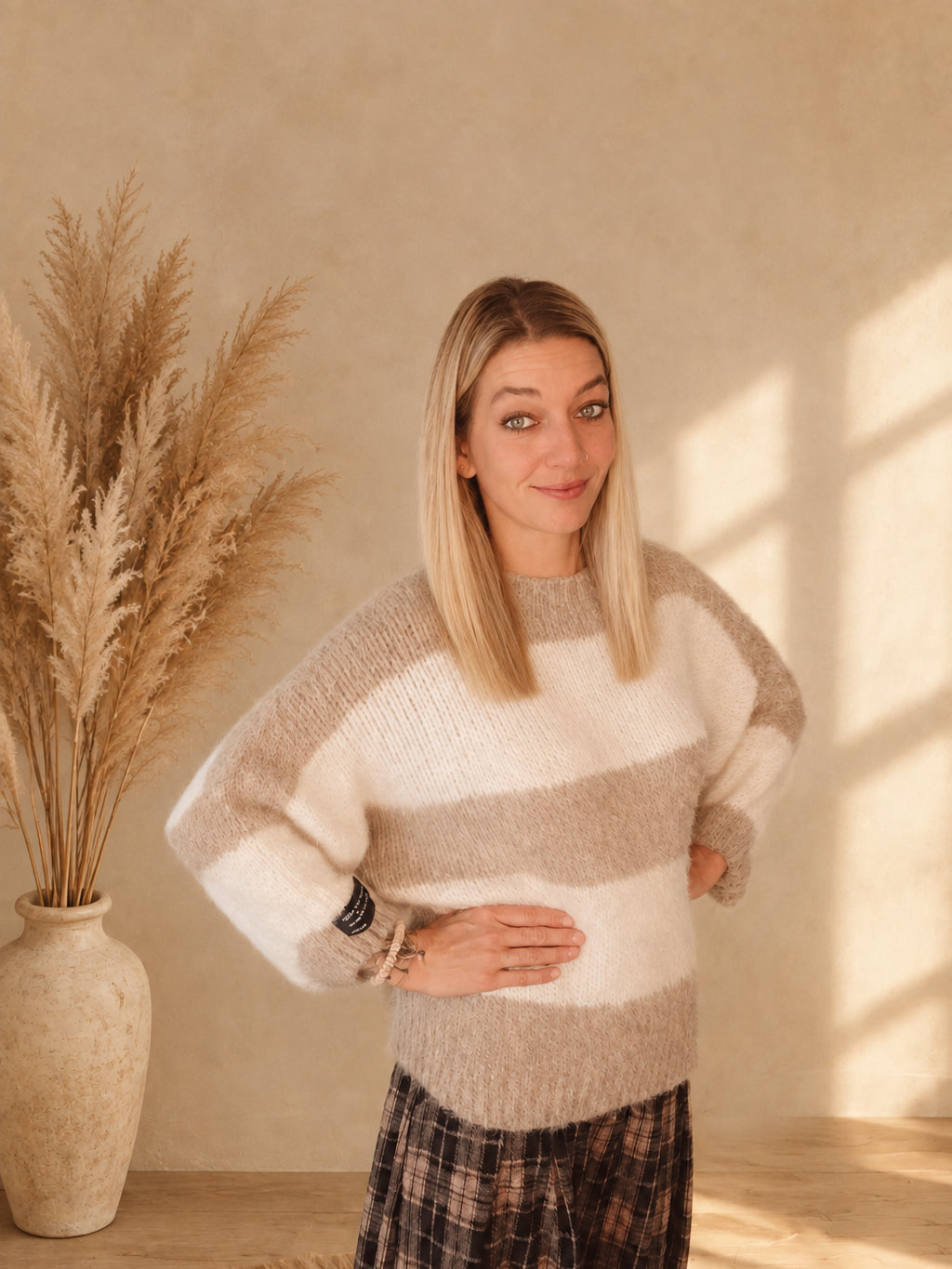 Damen-Strickpullover mit breiten Streifen in Beige und Creme, Rundhalsausschnitt und schwarzem Ärmelpatch, leicht seitliche Frontansicht am Model