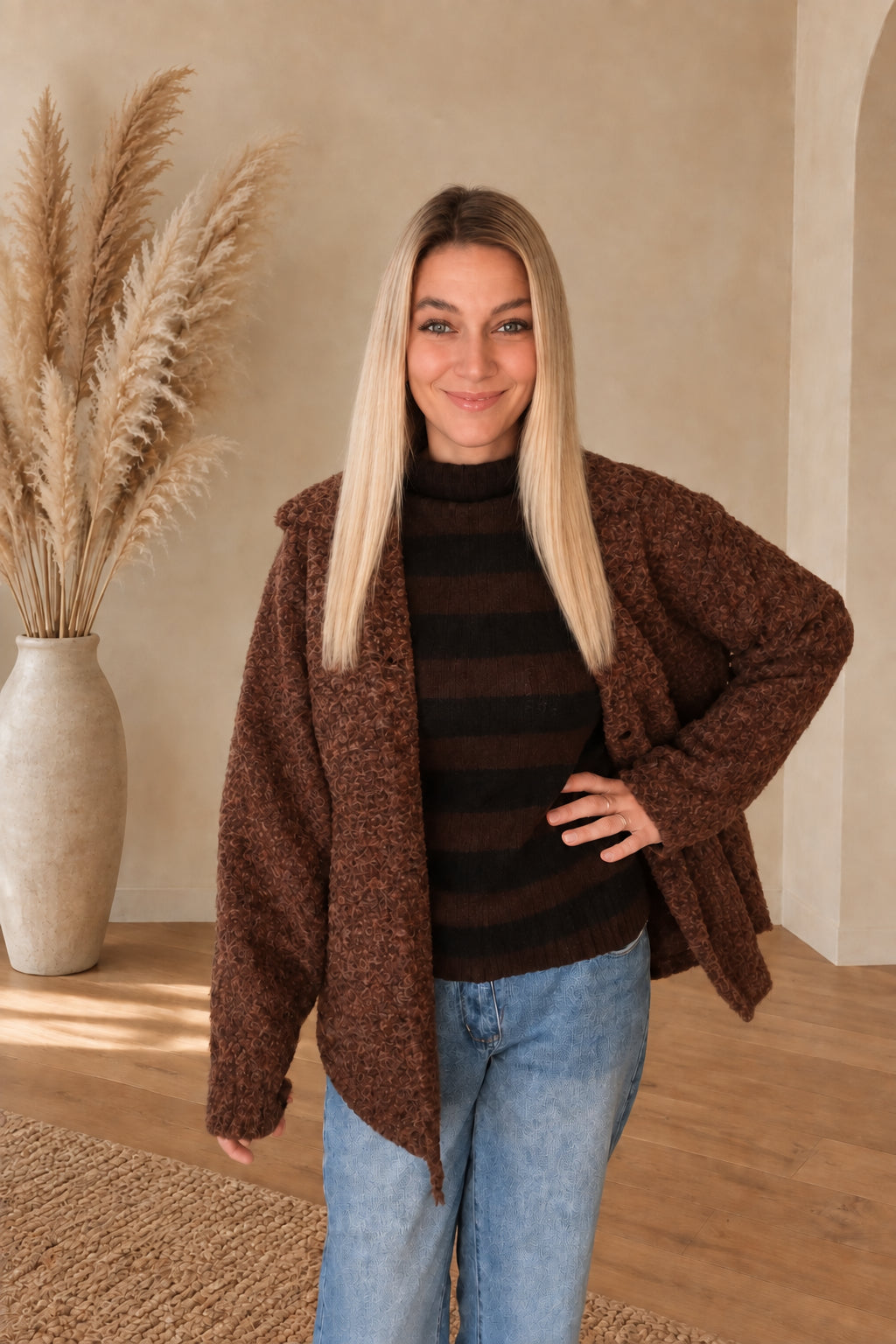 Braune Damenjacke mit strukturierter Oberfläche und weiten Ärmeln, offen getragen, eine Hand an der Hüfte.