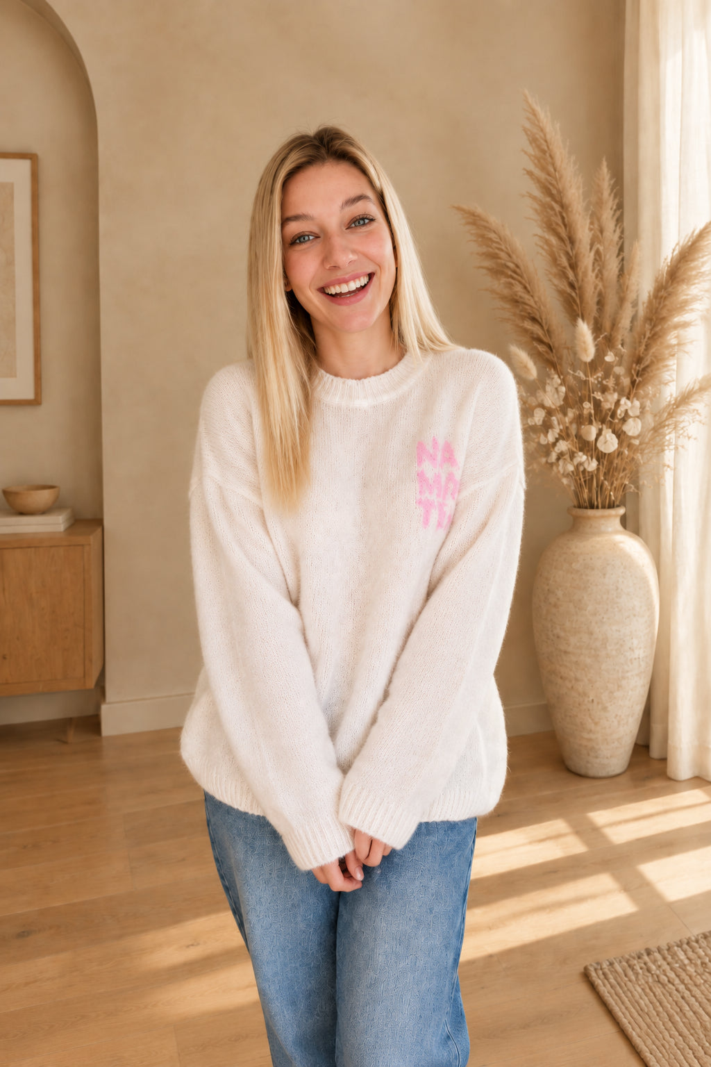 Cremeweißer Namasté-Pullover mit rosa Brustprint, am lächelnden Model mit vor dem Körper gehaltenen Händen.