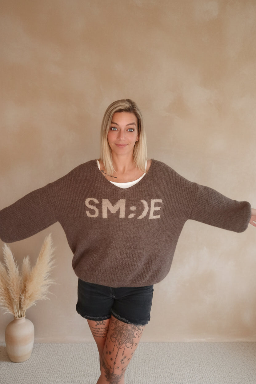 Boho-Luxe brauner Strickpullover mit V-Ausschnitt und Print kombiniert mit schwarzen Shorts.