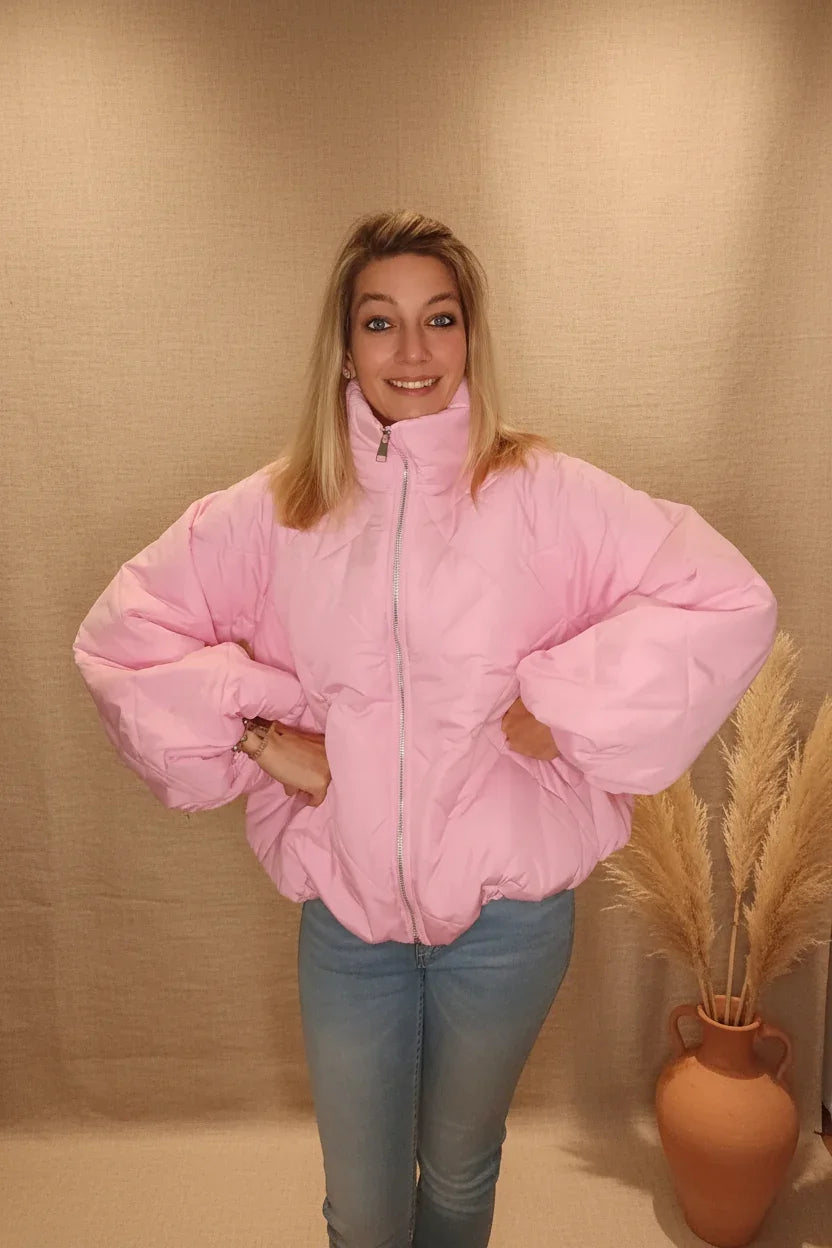 Frau in einer rosa gesteppten Oversize-Steppjacke aus glänzendem Material und Blue Jeans