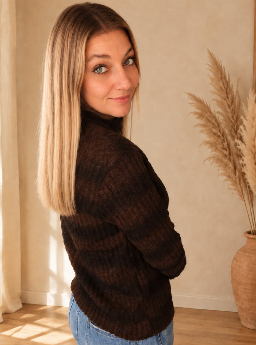Seitliche Rückansicht des dunkelbraun-schwarz gestreiften Strickpullovers, am Model mit Blick über die Schulter.