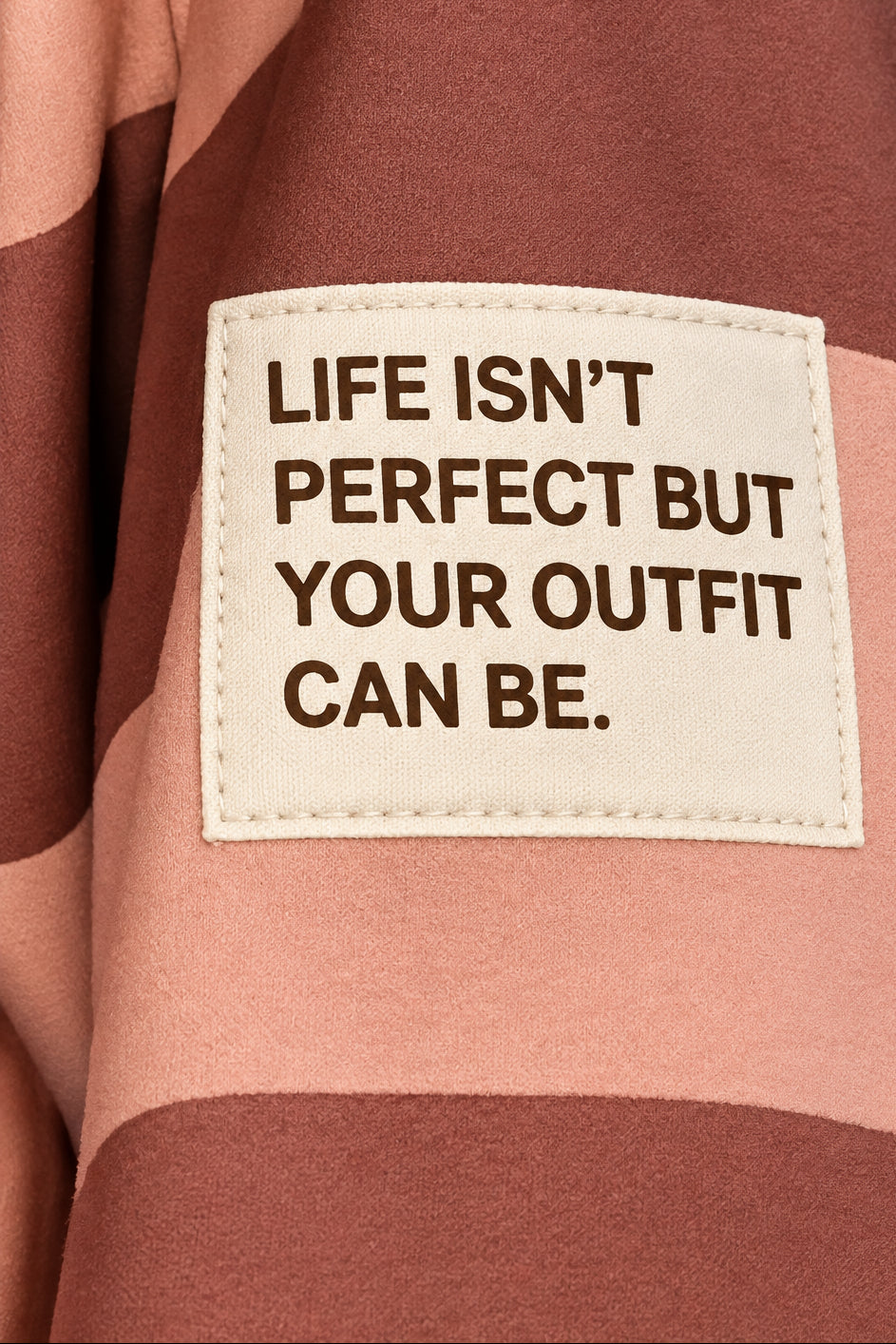 Nahaufnahme des Patches „Life isn’t perfect but your outfit can be.“ auf dem rosa-braun gestreiften Damen-Sweatshirt.