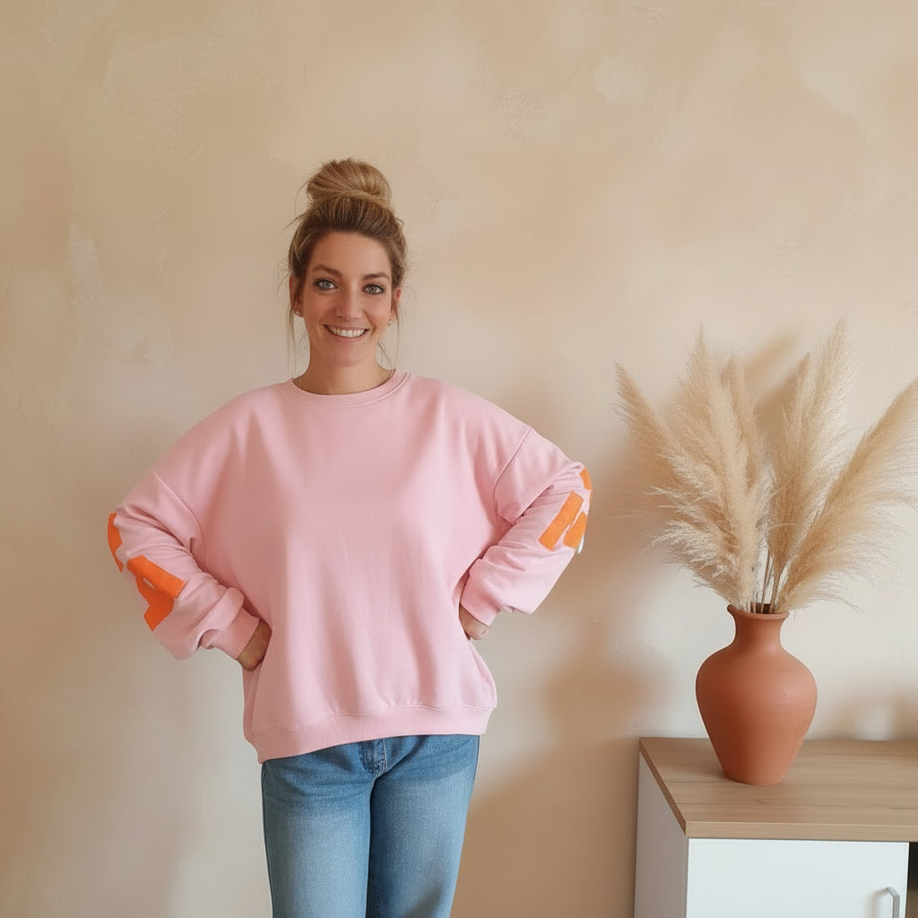 Rosa PARADISE-Sweatshirt mit orangefarbenem Ärmelprint, frontale Outfitansicht am Model mit Jeans