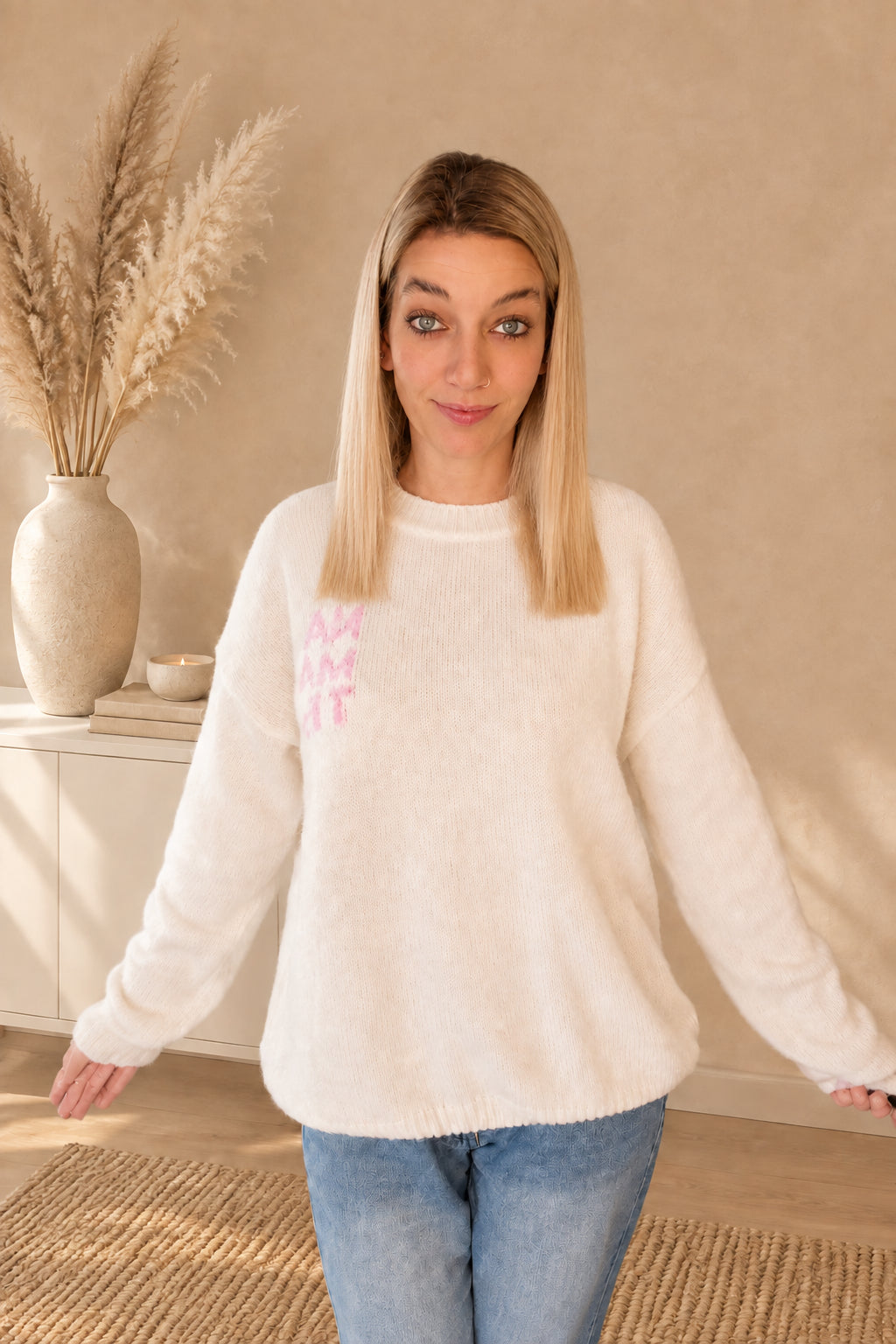 Cremeweißer Damenpullover mit Rundhalsausschnitt und rosa Namasté-Brustprint, am Model mit geöffneten Armen.