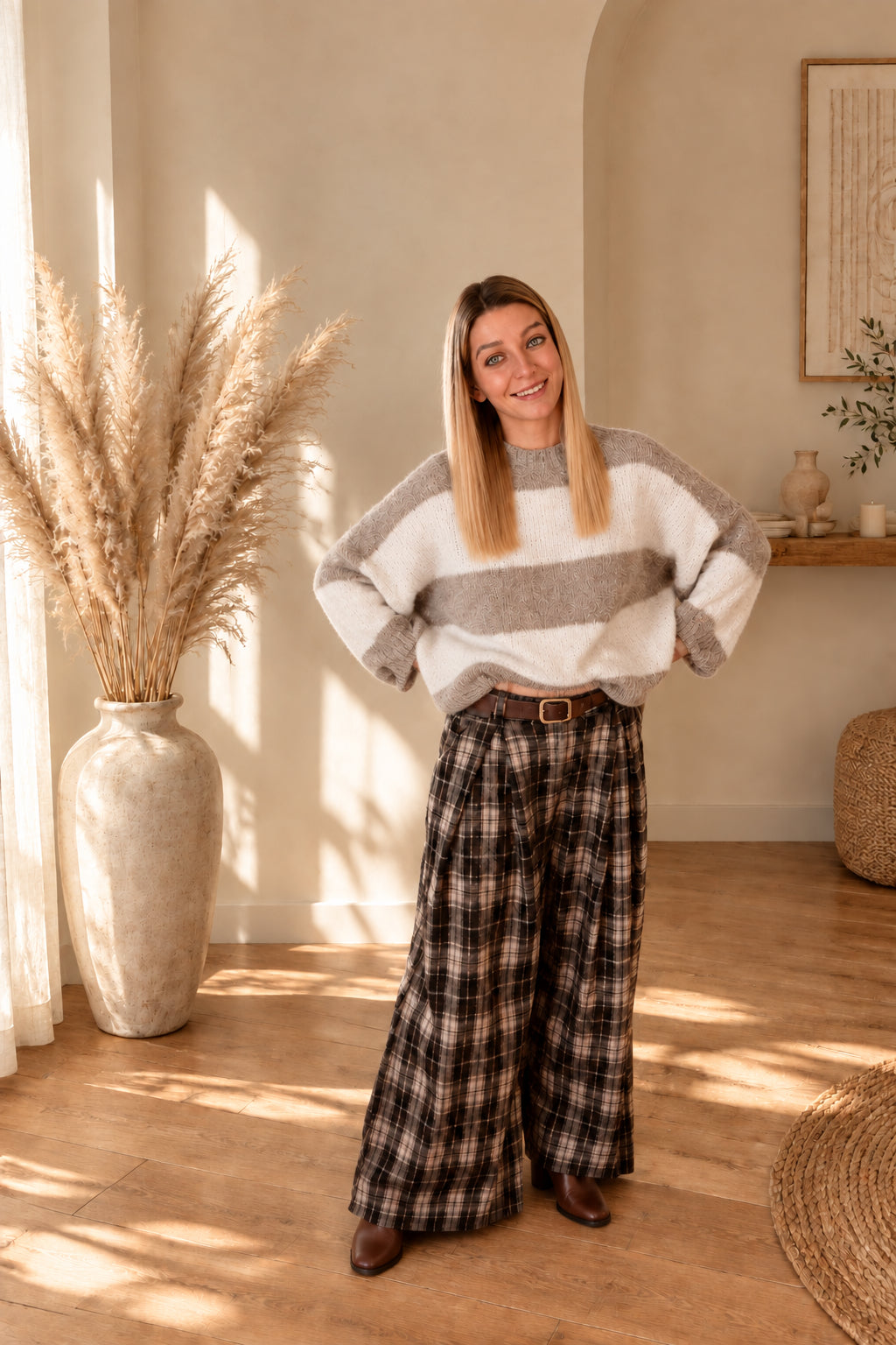 Karierte Damenhose mit weitem Bein und braunem Gürtel, kombiniert mit Streifenpullover und braunen Stiefeletten