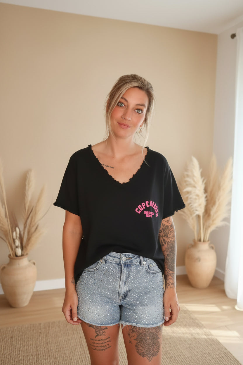 Boho-Luxe Look: Schwarzes V-Ausschnitt Shirt aus Baumwolle und hellblaue Jeansshorts mit Perlenbesatz.