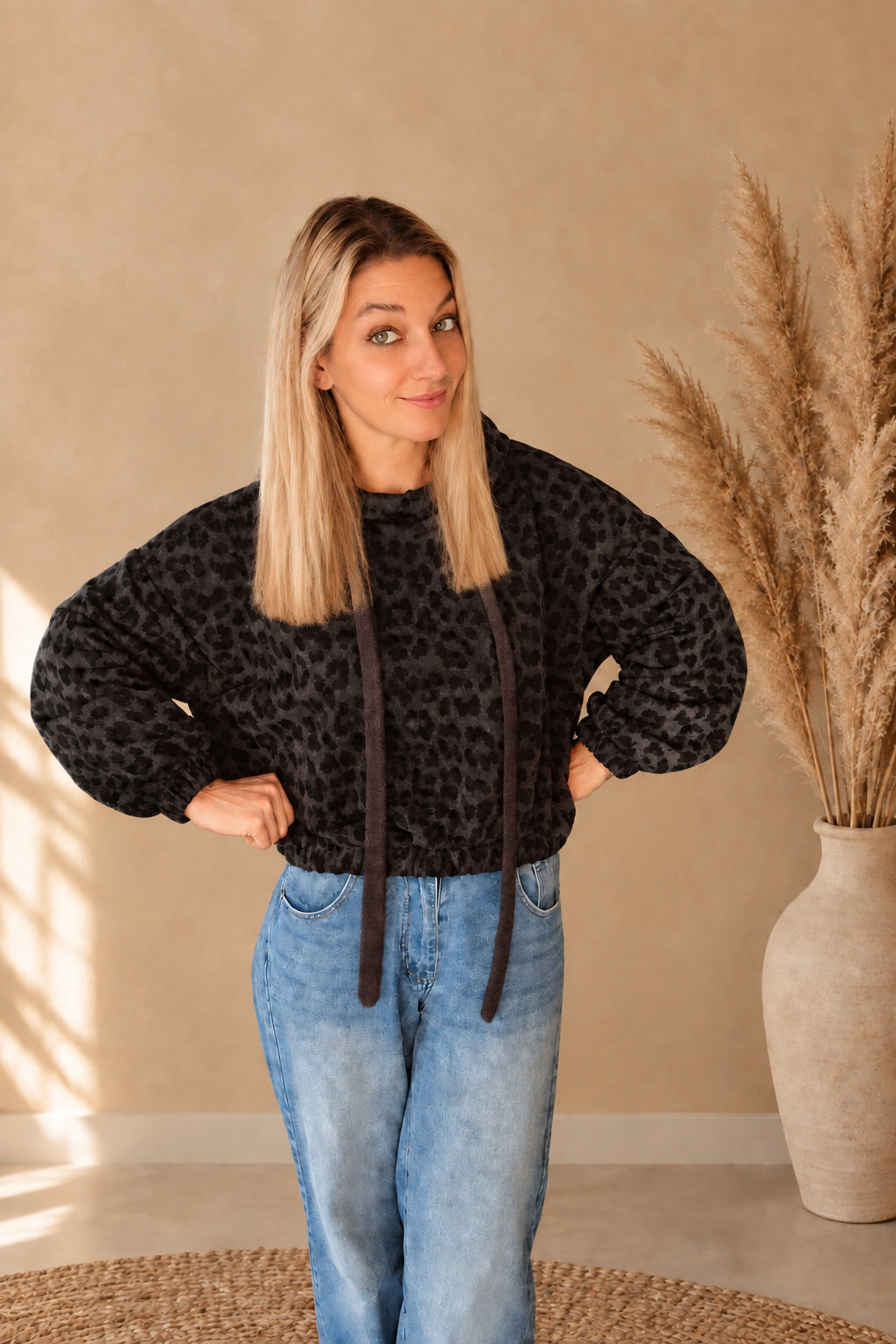Kurz geschnittener Damen-Hoodie mit Leopardenmuster und weiten Ärmeln, frontal am Model mit Händen an der Hüfte.